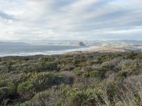 the view from a hilltop overlooking the ocean and land in the distance is hills, bushes and mountains