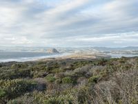 the view from a hilltop overlooking the ocean and land in the distance is hills, bushes and mountains