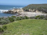 an ocean beach and cliffs with a lone blue chair on the ground near water and grass