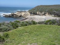 an ocean beach and cliffs with a lone blue chair on the ground near water and grass