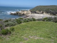 an ocean beach and cliffs with a lone blue chair on the ground near water and grass