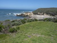 an ocean beach and cliffs with a lone blue chair on the ground near water and grass