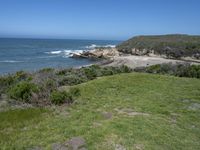 an ocean beach and cliffs with a lone blue chair on the ground near water and grass