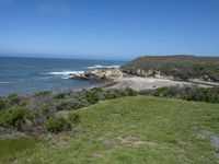 an ocean beach and cliffs with a lone blue chair on the ground near water and grass