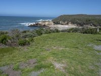 an ocean beach and cliffs with a lone blue chair on the ground near water and grass