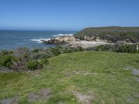 an ocean beach and cliffs with a lone blue chair on the ground near water and grass