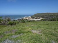 an ocean beach and cliffs with a lone blue chair on the ground near water and grass