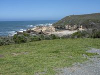 an ocean beach and cliffs with a lone blue chair on the ground near water and grass