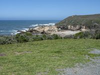 an ocean beach and cliffs with a lone blue chair on the ground near water and grass