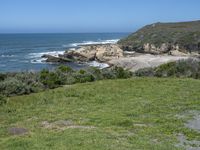 an ocean beach and cliffs with a lone blue chair on the ground near water and grass