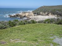 an ocean beach and cliffs with a lone blue chair on the ground near water and grass