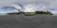 a fisheye photo of a circular road with some houses in the background and people standing on the shore