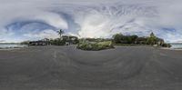 a fisheye photo of a circular road with some houses in the background and people standing on the shore