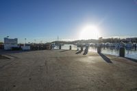 a dock at the water's edge with the sun shining in the background and many boats in the marina