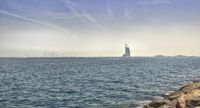 sail boats are seen sailing on the water near rocks and buildings in the background during sunny day