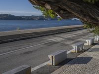 a man is throwing a ball into the air over the sidewalk near a river, on a sunny day