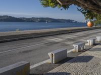 a man is throwing a ball into the air over the sidewalk near a river, on a sunny day