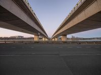 two highway bridges span across the empty asphalt road in a city near the water and buildings