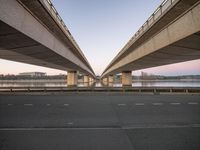 two highway bridges span across the empty asphalt road in a city near the water and buildings