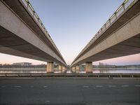 two highway bridges span across the empty asphalt road in a city near the water and buildings