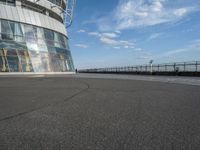 the ground is covered in asphalt and is next to an observation tower, with buildings reflected in the window windows