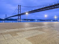 view of a bridge spanning a wide body of water at night time with lights in foreground