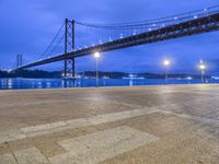 view of a bridge spanning a wide body of water at night time with lights in foreground