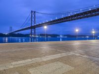 view of a bridge spanning a wide body of water at night time with lights in foreground