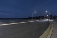 an empty street near the water under cloudy skies at night hours with one light turned on