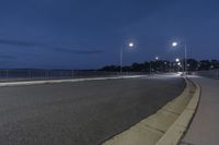 an empty street near the water under cloudy skies at night hours with one light turned on