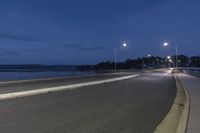 an empty street near the water under cloudy skies at night hours with one light turned on