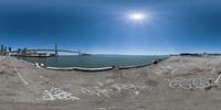 a fish eye view of an ocean with graffiti writing on it and a bridge in the background