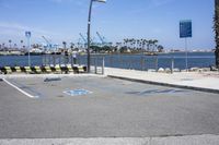 a parking lot with two lanes that are marked in blue paint on the street, and three benches near the ocean