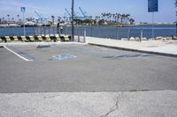 a parking lot with two lanes that are marked in blue paint on the street, and three benches near the ocean