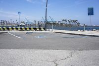 a parking lot with two lanes that are marked in blue paint on the street, and three benches near the ocean