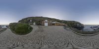 two stoned pavement walkways with benches and buildings on a hill by the ocean