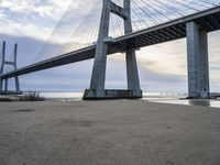 the big bridge is near the water and the sand is empty with no one around it