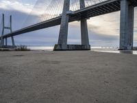 the big bridge is near the water and the sand is empty with no one around it