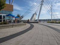 a sidewalk by the water with people walking and sitting on tables near a boat sculpture