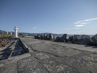 a lighthouse is sitting at the side of a path by some rocks in a harbor