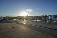 a group of people walking across a street at sunset in front of a lot of boats