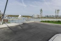 a parking lot with a fence near the water and buildings in the background that includes several boats