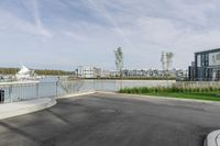 a parking lot with a fence near the water and buildings in the background that includes several boats