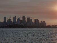 an ocean view of a skyline and skyscrapers at sunset in the background, including an airplane