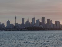 an ocean view of a skyline and skyscrapers at sunset in the background, including an airplane