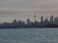 an ocean view of a skyline and skyscrapers at sunset in the background, including an airplane