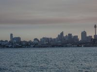 an ocean view of a skyline and skyscrapers at sunset in the background, including an airplane