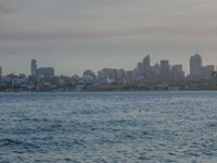 an ocean view of a skyline and skyscrapers at sunset in the background, including an airplane