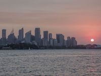 an ocean view of a skyline and skyscrapers at sunset in the background, including an airplane