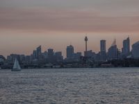 an ocean view of a skyline and skyscrapers at sunset in the background, including an airplane